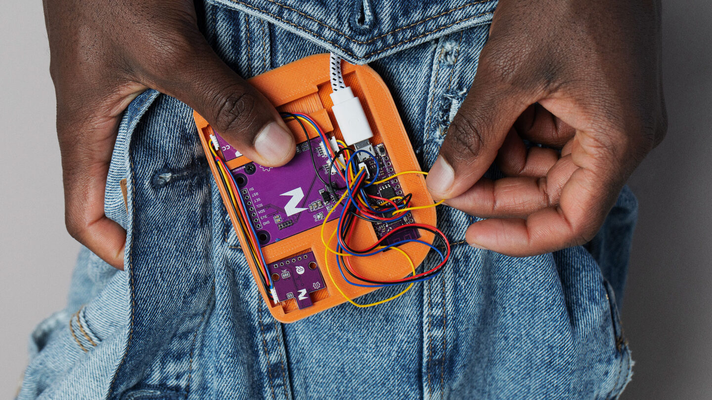 Mains tenant un appareil électrique orange ouvert sur une veste en jean.