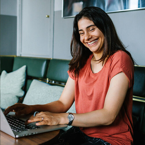 Nuori naispuolinen työntekijä hymyilee työskennellessään kannettavan tietokoneen ääressä.