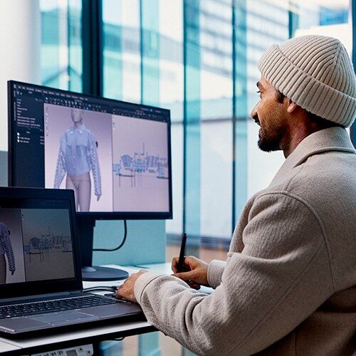 Vīrietis sēž pie datora, datora ekrānā redzams jakas 3D dizains.