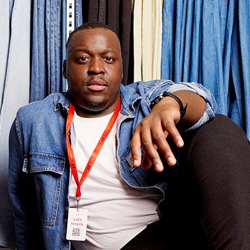 Male store employee looking into the camera with a confident expression. Stood in front of lots of denim.